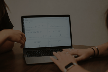 ACBM Blog Feature Image: How to Avoid Downloading Data from JDE into Excel for Reporting : Laptop with dashboard opened and people doing reporting